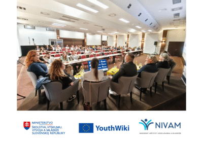 ilustračná fotografia z konferencie. Vpredu sedia hostia hovoriaci do mikrofónu, v pozadí obecenstvo